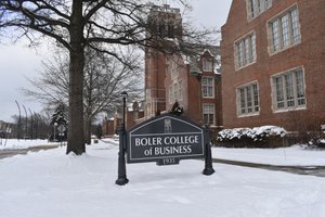 A snow-covered campus scene shows a black sign reading Boler College of Business in front of a red brick building and