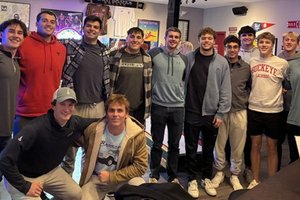 A group of twelve young men pose closely together smiling inside a room decorated with sports memorabilia and signs.