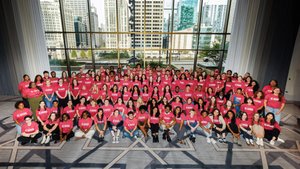 A large group of students gathers together in a grand ballroom, smiling for a photo; city skyscrapers are visible through