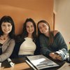 Three young women sit closely together at a wooden table in a restaurant, smiling at the camera.