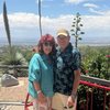 Two people, a man and a woman, smile while posing for a picture on an outdoor patio overlooking a vast landscape.