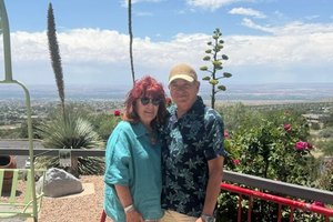 Two people, a man and a woman, smile while posing for a picture on an outdoor patio overlooking a vast landscape.