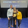 Three people stand smiling in front of a screen that reads welcome to 2024 John Carroll Athletics Hall of Fame.