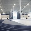 A large indoor sports facility with a blue running track curving around a multi-use court under bright ceiling lights.