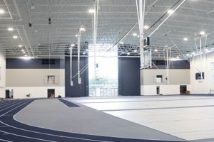 A large indoor sports facility with a blue running track curving around a multi-use court under bright ceiling lights.