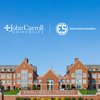 A large red brick university building with multiple windows and a sign reading John Carroll University under a clear blue.