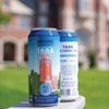 Two cold cans of Great Lakes Brewing Co. 1886 John Carroll Lager sit on a white ledge with a blurred brick building in the