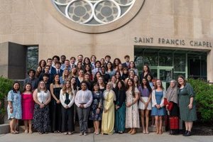A large group of people posing and smiling in front of a building labeled Saint Francis Chapel.