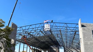 A steel framework is being lifted into place by two cranes at a construction site with a banner reading Building Inspired.