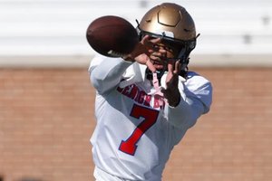 A football player wearing a gold helmet and white jersey with number seven reaches out to catch a football in midair.