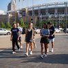 Five students walk together near a ballpark; two wear university branded shirts.