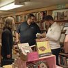 Three people browse books at an off-campus used bookstore. One person is looking at a book, and one is holding a phone.
