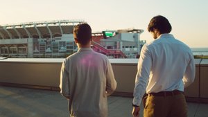 Two students walk away from the viewer, outside near a stadium, bathed in the warm glow of sunset.