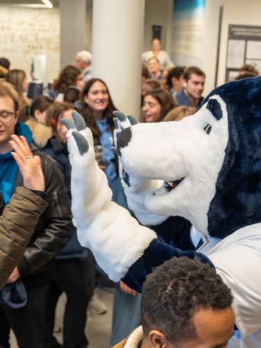 A person in a husky mascot costume high-fives a smiling woman in a crowded indoor space.