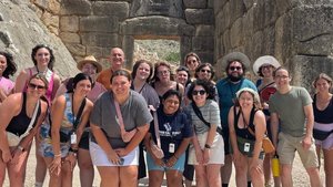 A group of people posing and smiling in front of an ancient stone gateway with carved lions under a blue sky.