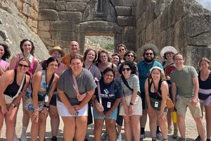 A group of people posing and smiling in front of an ancient stone gateway with carved lions under a blue sky.