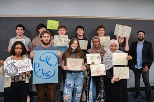 A diverse group of eleven people stand in front of a blackboard holding colorful handwritten signs with artistic designs and