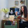 A cheerful JCU student with curly hair sits at a well-lit desk, holding a notebook and pen, focused on their studies.