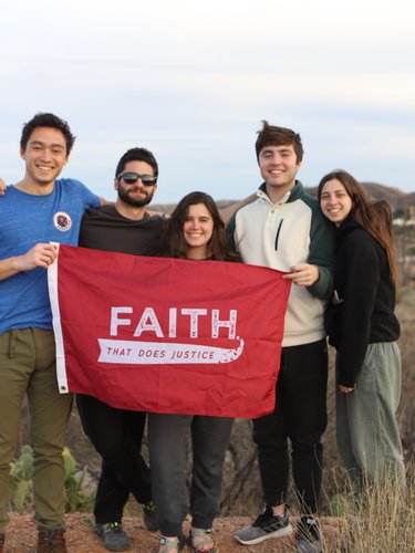 Five young adults stand outdoors on a hill holding a red flag that reads "FAITH THAT DOES JUSTICE.