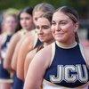 A group of five cheerleaders in navy and gold uniforms stand in a line on a track, with the closest one smiling.