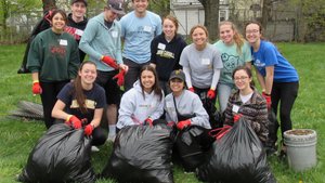 A group of twelve young adults wearing gloves pose outdoors with large black trash bags filled with collected debris.