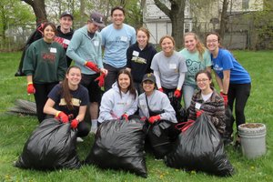 A group of twelve young adults wearing gloves pose outdoors with large black trash bags filled with collected debris.