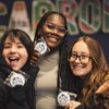 Three smiling young women hold up cookies with a blue paw print design in front of a colorful CARROLL sign.