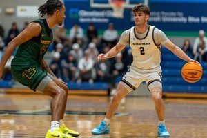 A basketball player in a white uniform dribbles the ball while being closely guarded by a player in a green uniform.
