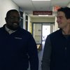 Two men walk down a hallway smiling and looking at each other near a Student Service sign.