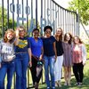 Seven young women stand smiling together in front of a metal gate that reads Ohio City Farm on a sunny day.