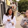 Two young women wearing John Carroll University hoodies laugh while eating ice cream outside on a sidewalk.