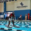 A person wearing a helmet and mask balances on two floating platforms in a swimming pool at John Carroll University.