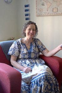 A smiling woman with curly hair sits in a red armchair, looking directly at the viewer with a warm expression.
