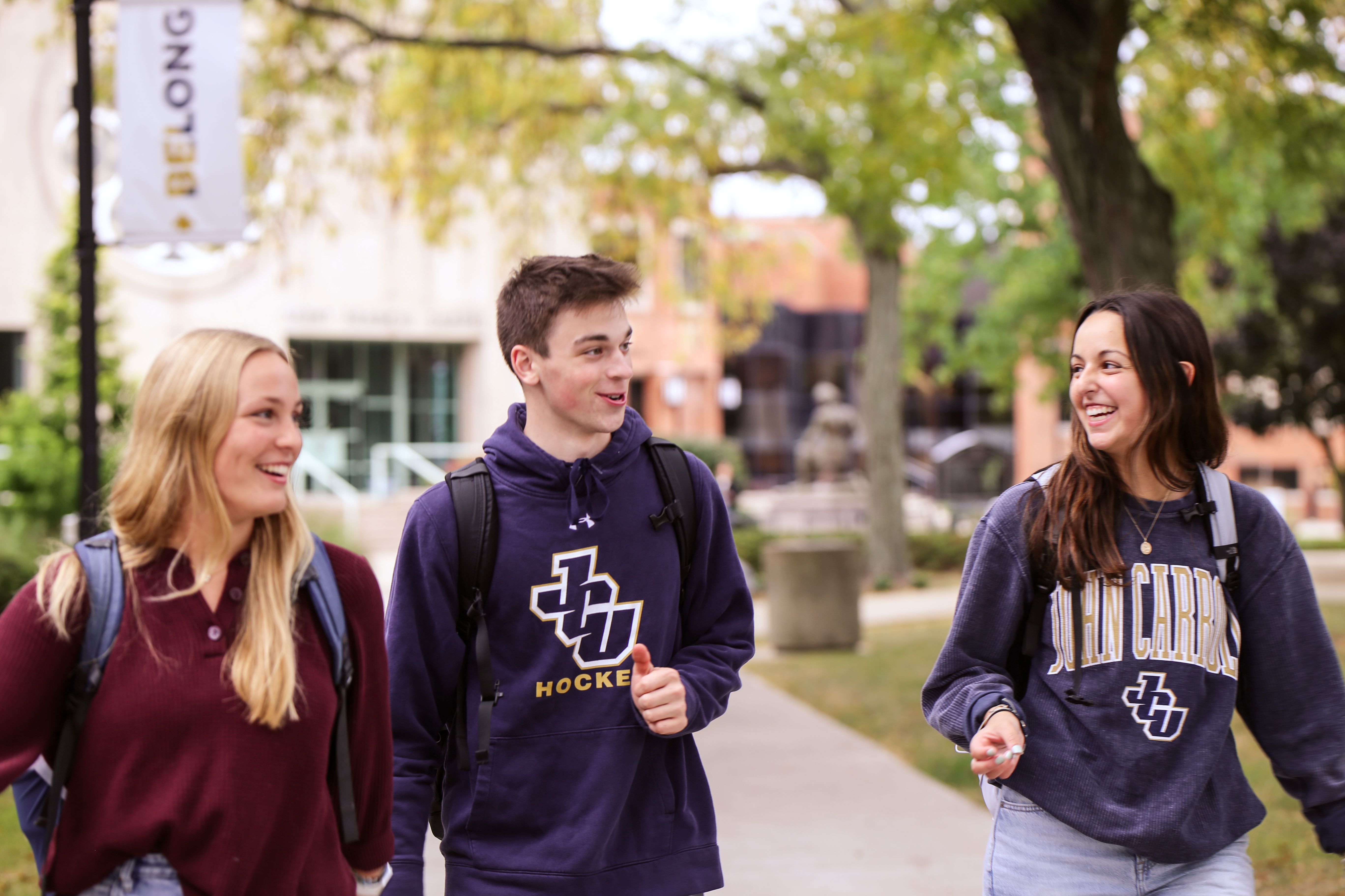 Three students walking on campus in front of student center