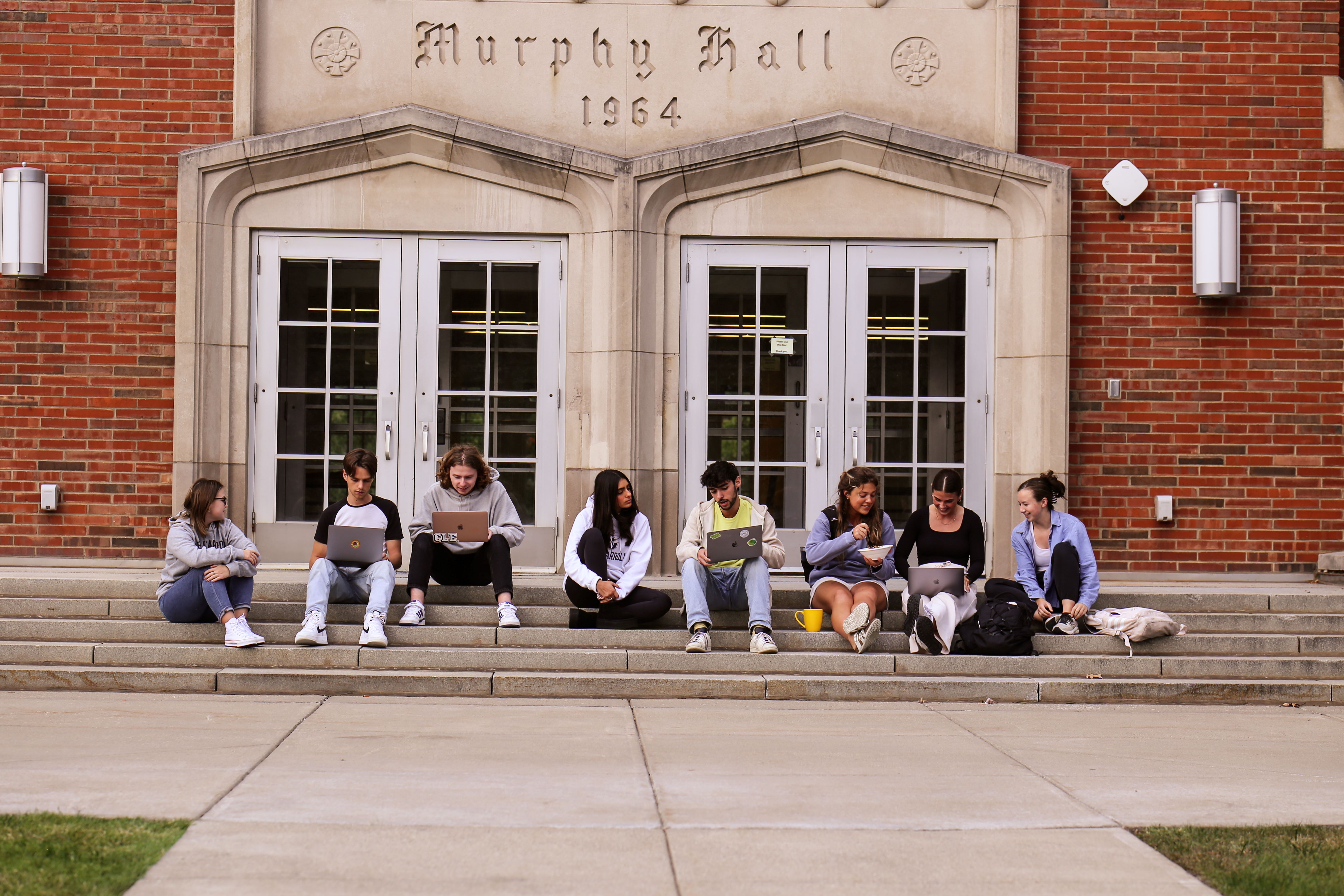 students on the steps of a residence hall exterior
