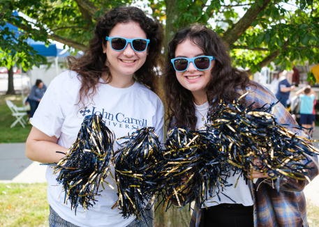 two female students waving JCU pom poms at homecoming game