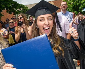 Happy female graduate giving a thumbs up in one hand and holding her diploma in the other