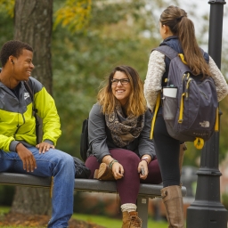 One male and two female students talking on a bench near the quad in the fall