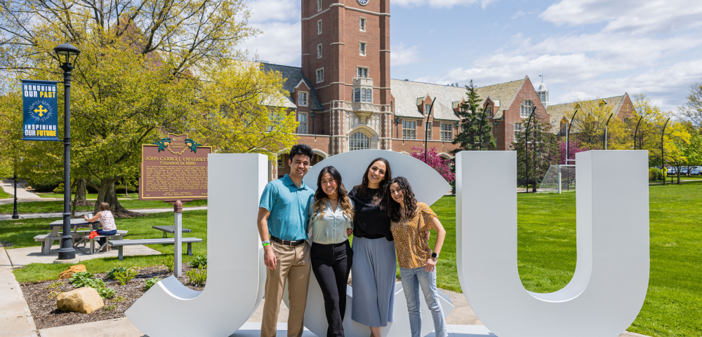 Four students standing close and smiling in front of big letters spelling JCU