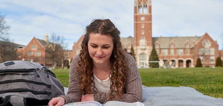 Female student studying on the quad with the Grasselli Clock Tower in the background