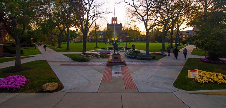 Campus photo at dusk showing the statue of St. Ignatius with the tower in the background and spring flowers everywhere 