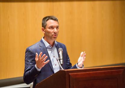 Tom Telesco stands at a podium and gestures during his lecture. 